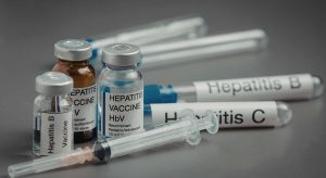 Close-up of vaccine vials labeled Hepatitis B and other vaccines with syringes on a gray background.
